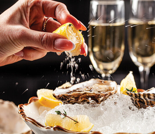 Prosecco Bar Concept. Open Oysters Lie On Crushed Ice With Lemon And Lime, Next To A Glass Of Champagne. Background Image. Copy Space.